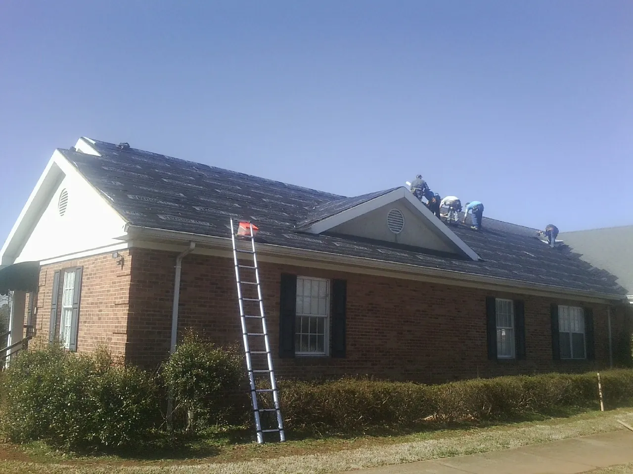 Crew tearing shingles off a brick ranch roof with a ladder set — Metal Roof Repair work by our crew in Kingston Springs