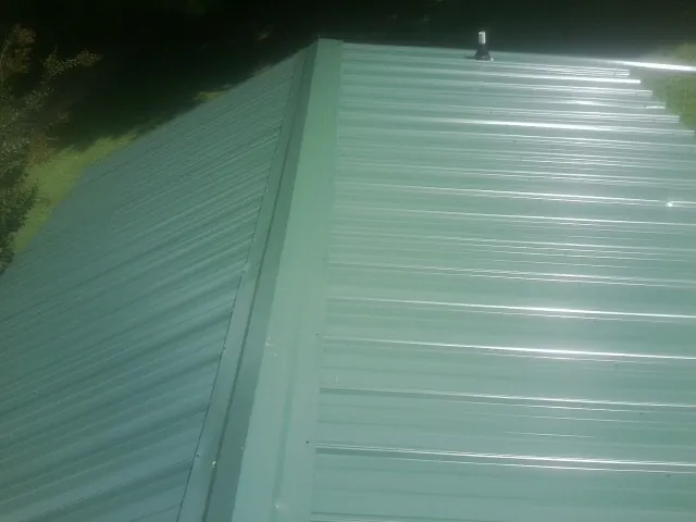 New green metal panels meeting at the ridge of a roof — Flat Roof Repair work by our crew in Kingston Springs
