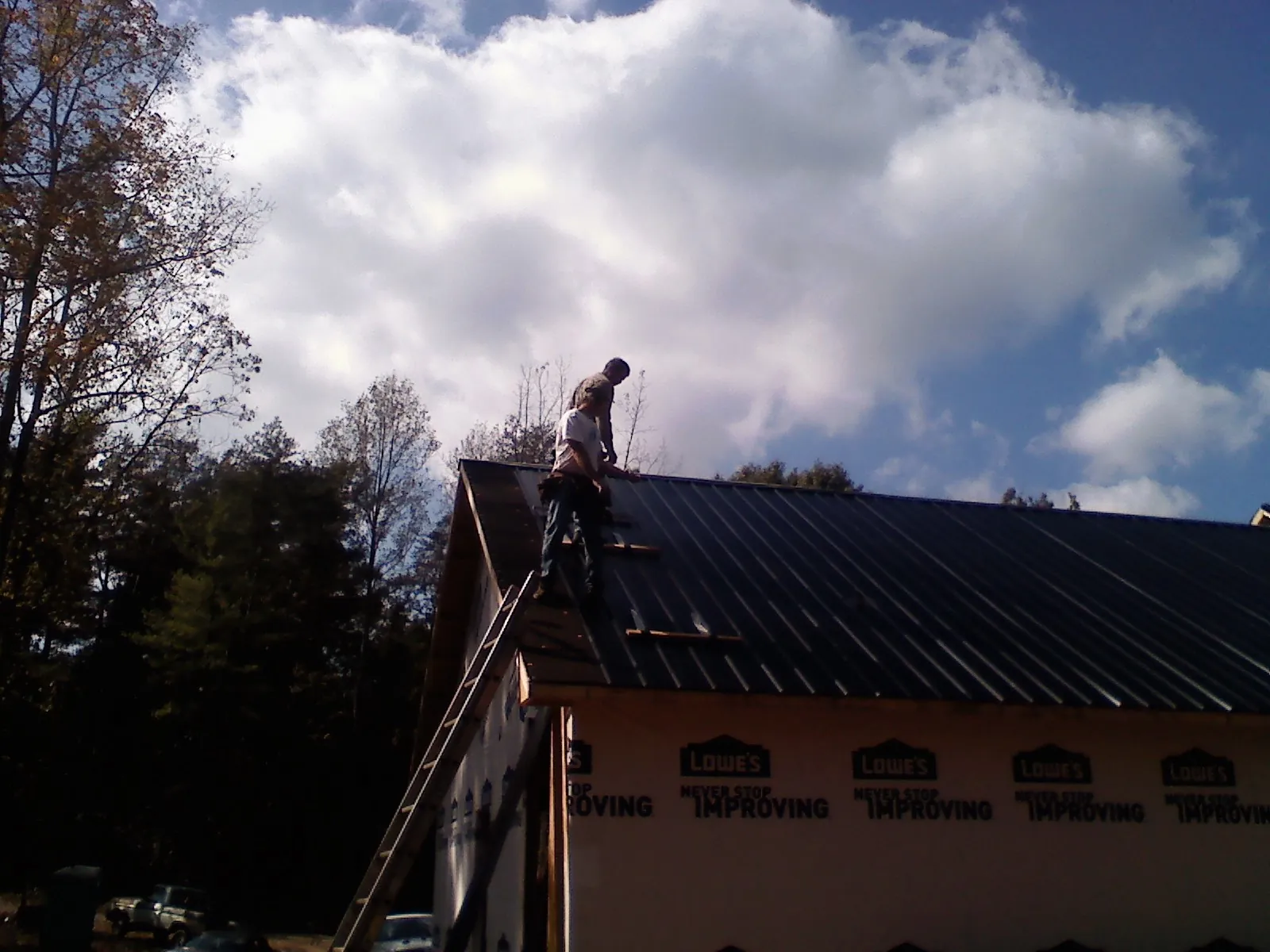 Roofer fastening dark metal panels high against a cloudy sky, from a Roof Inspection job in Kingston Springs