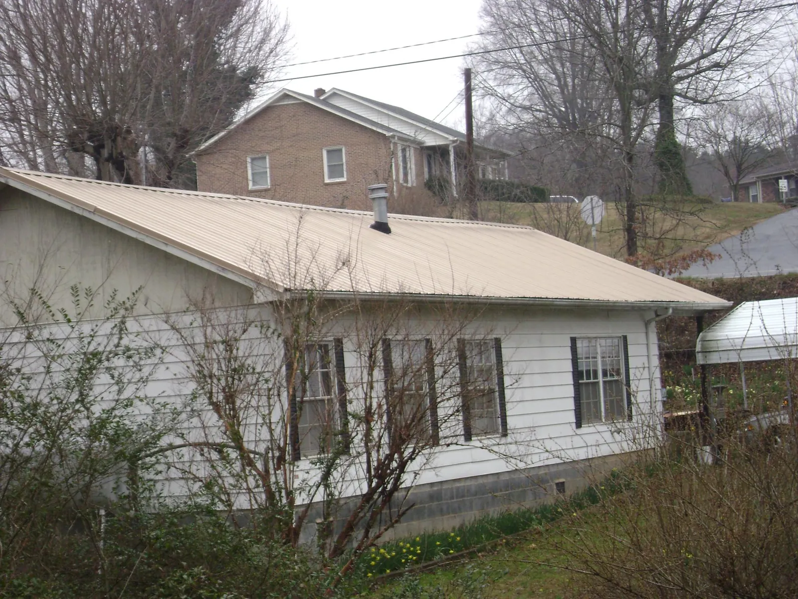 Tan metal roof on a white sided house set into a hillside — Commercial Roofing by Roofing Brothers in Kingston Springs