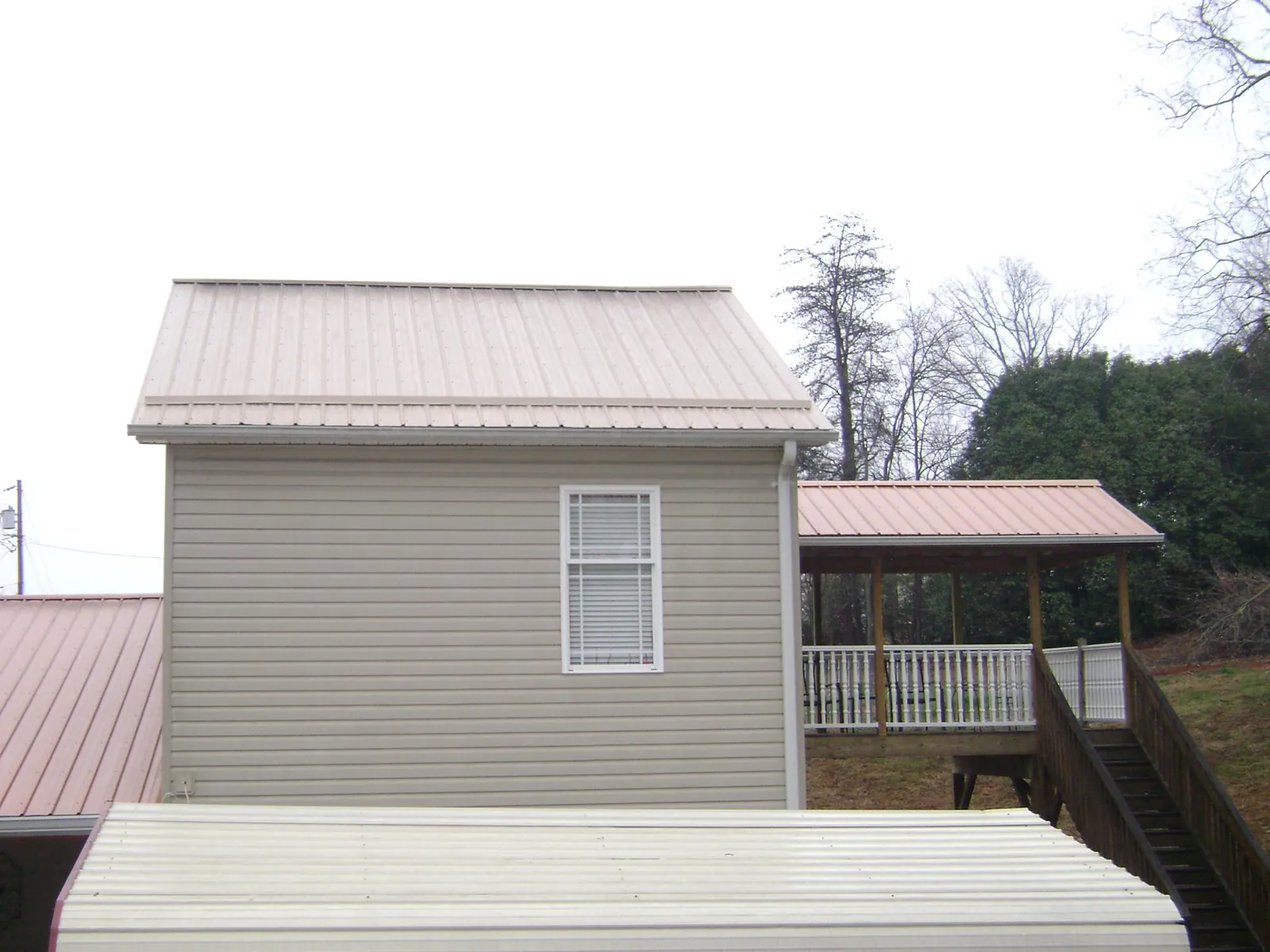 Tan metal roofs on a two story addition and attached porch, from a Roof Replacement job in Kingston Springs